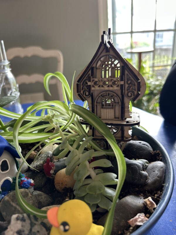 Assembled DIY fairy and elf house kit made from 3mm basswood, displayed in a garden planter with whimsical fairy decor