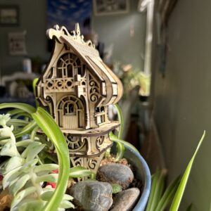 Assembled DIY fairy and elf house kit made from 3mm basswood, displayed in a garden planter with whimsical fairy decor