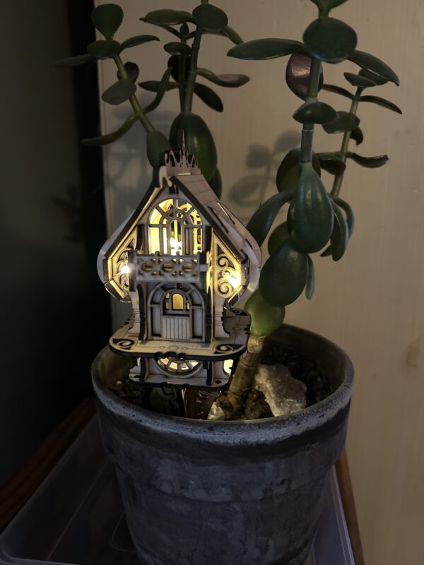 Assembled DIY fairy and elf house kit made from 3mm basswood, displayed in a garden planter with whimsical fairy decor